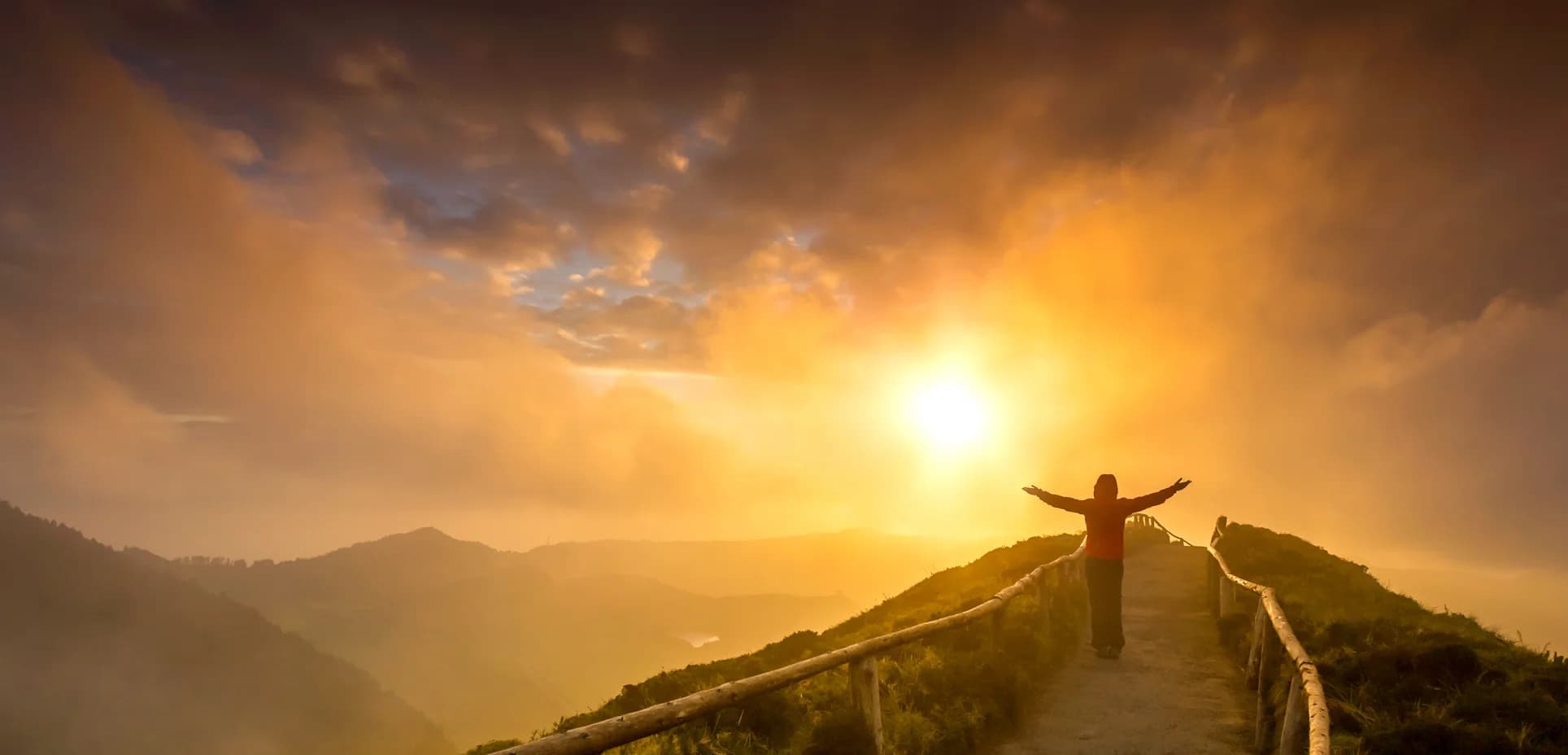 A person with arms outstretched on a mountain path at sunrise