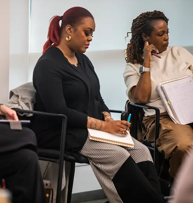 Two students take notes during a class discussion