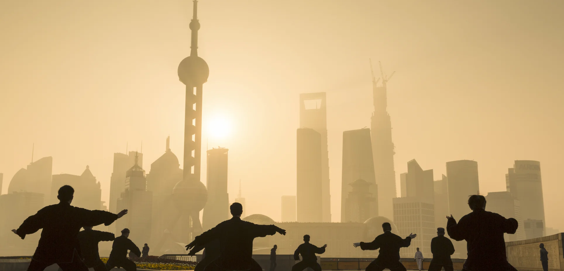 People practicing tai chi in silhouette before a city skyline at sunrise
