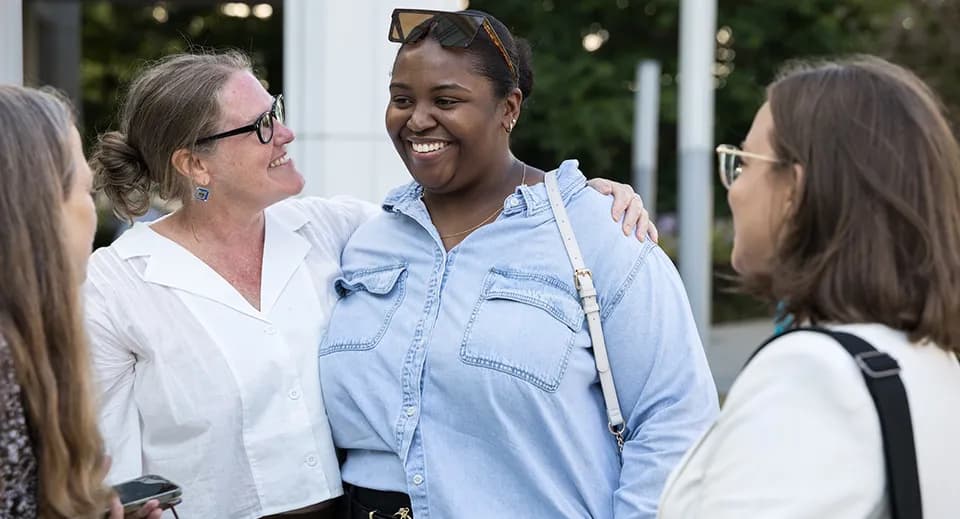 Three smiling students standing together in conversation on the university campus