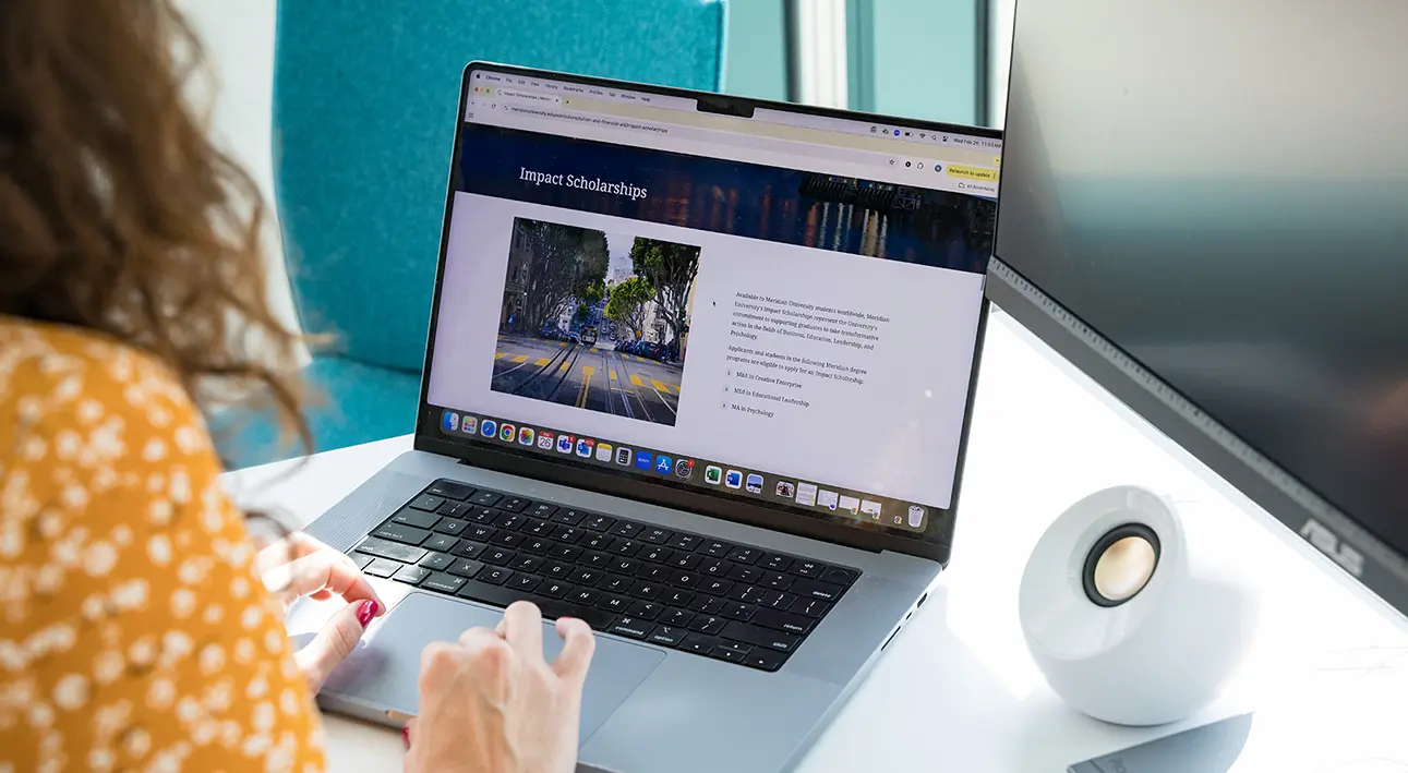 young woman sits behind laptop and book doin research in library