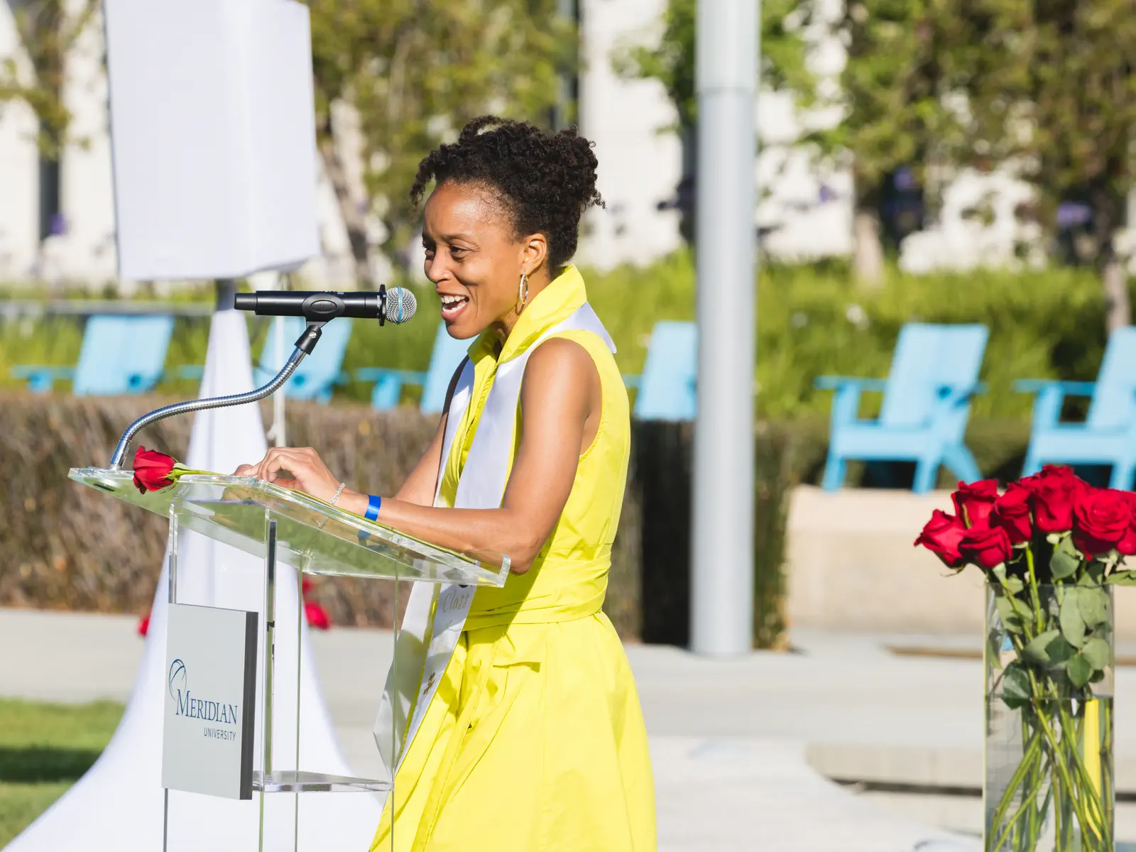 A woman in a yellow dress and white stole speaks at a Meridian University podium