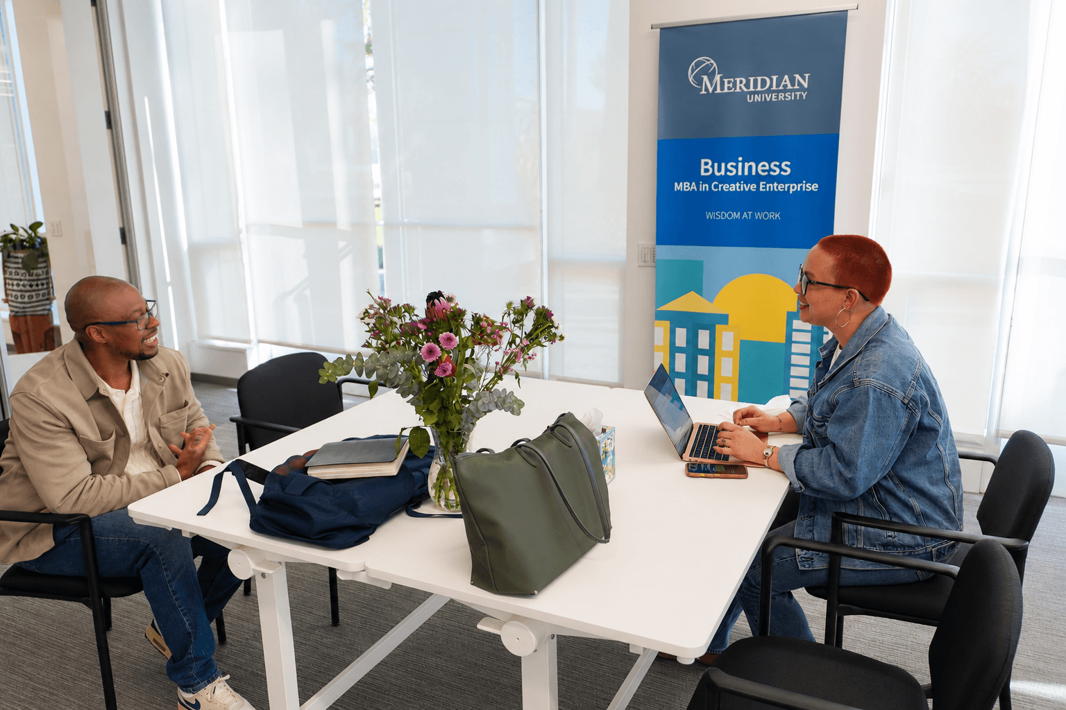 Two people sitting at a table talking at Meridian University campus