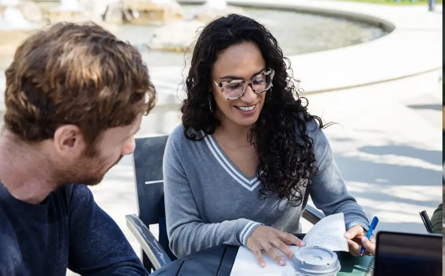Two people in an outdoor conversation reviewing notes together at a table.