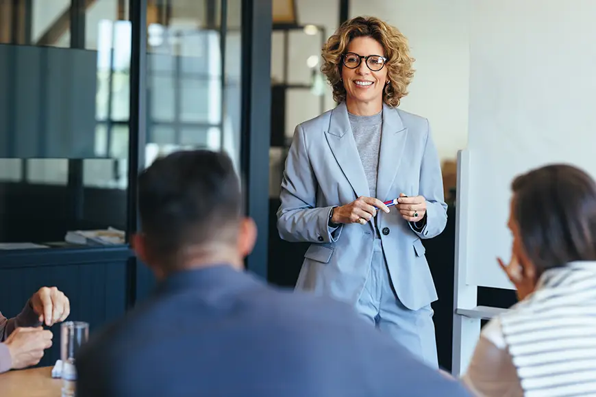 A businessperson in a suit smiles as they discuss a project with their team