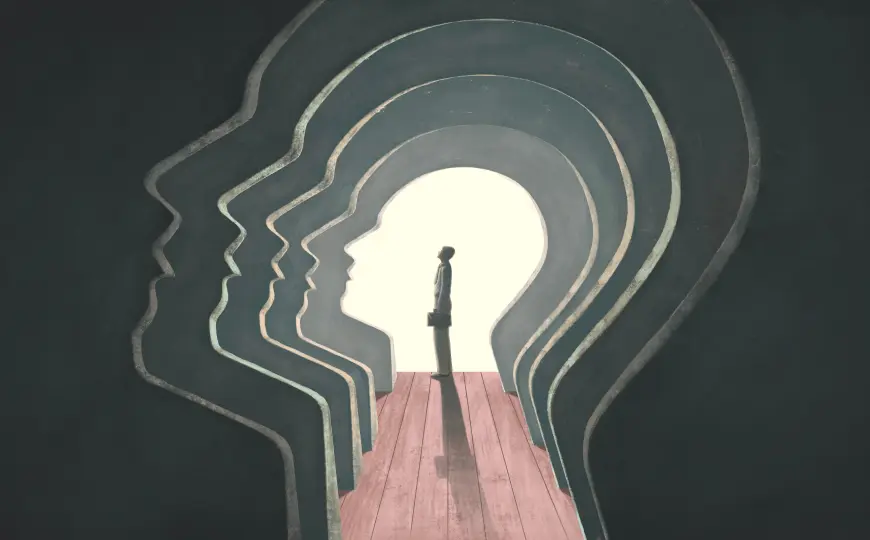 A lone figure stands in a bright opening framed by multiple-layered human profiles, creating the impression of walking through the contours of the mind.
