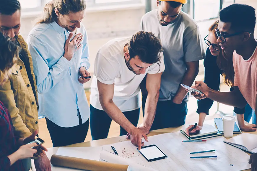 A business startup team works together while standing around a table.