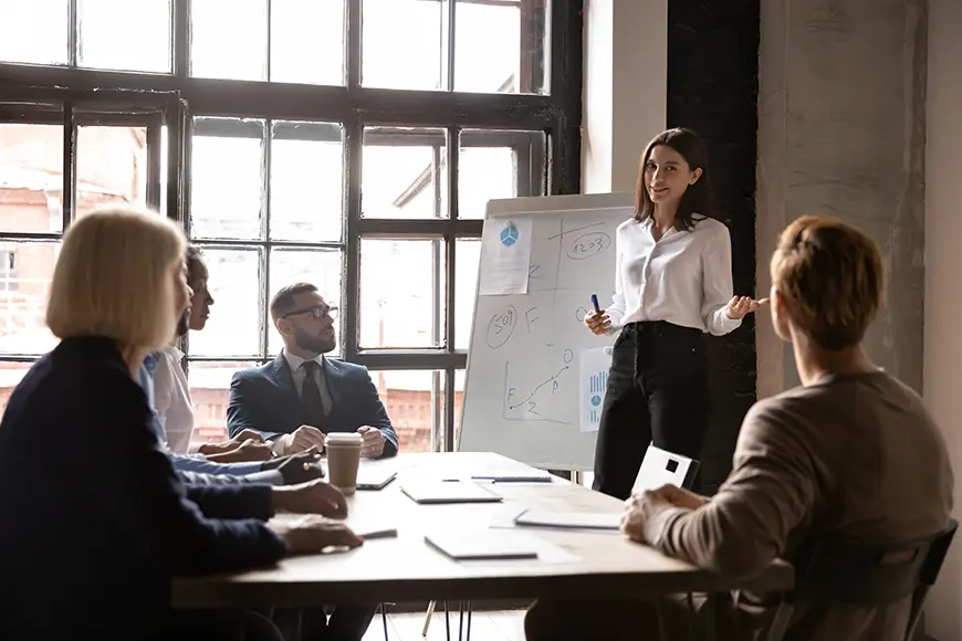A woman is holding a presentation in front of several people during an office meeting.