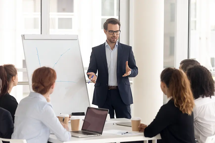 A man is holding a presentation in front of several people during an office meeting.