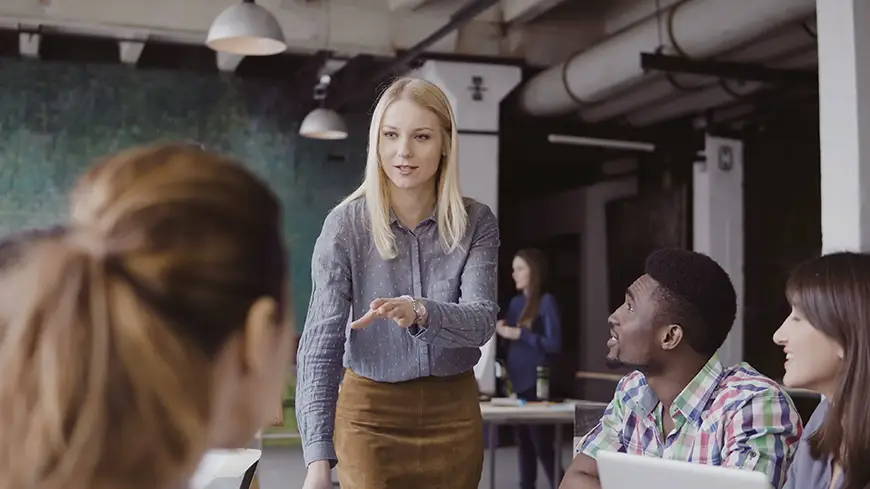 A woman dressed in business attire assigns tasks to her team members at a table