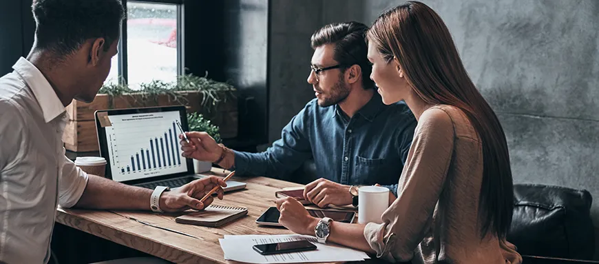 A group of three people, two men, and a woman analyze a graph on a computer.